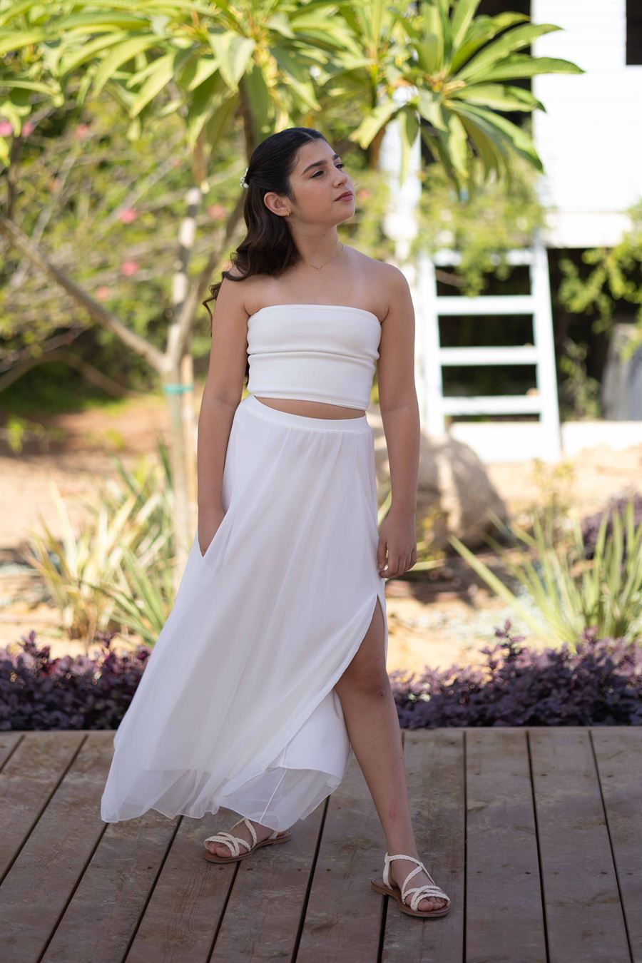Young girl in a white dress photographed outdoors for a milestone portrait.